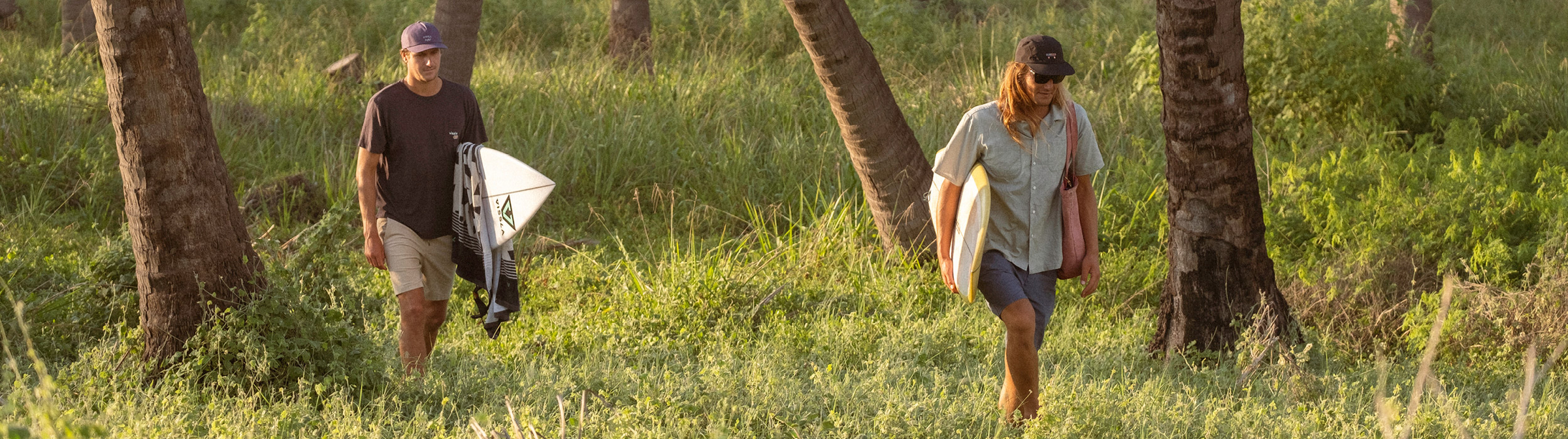 Two Vissla Surfers wearing eco friendly and sustainable walkshorts holding their surfboards and heading through a tropical forest