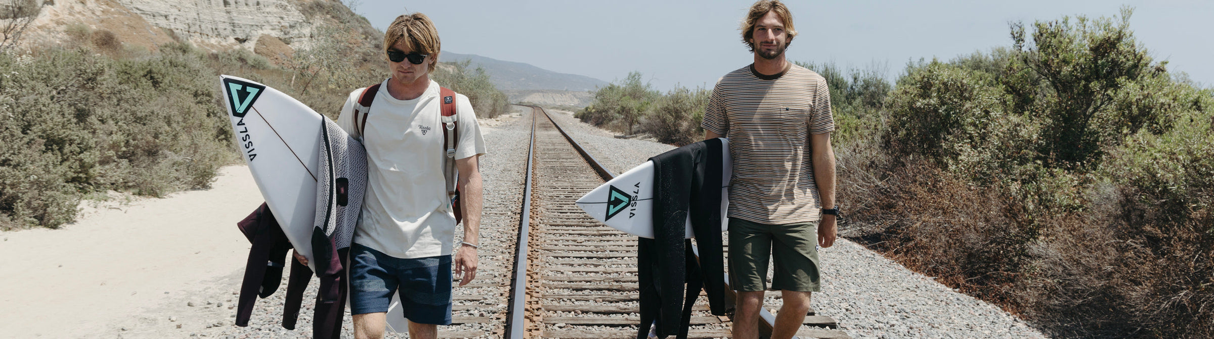 a surfer wearing Vissla Sofa Surfer Shorts standing near the shore next to a white picket fence