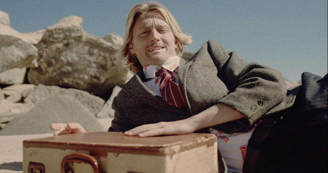 Josiah Amico laying on beach in suit with box in front of him