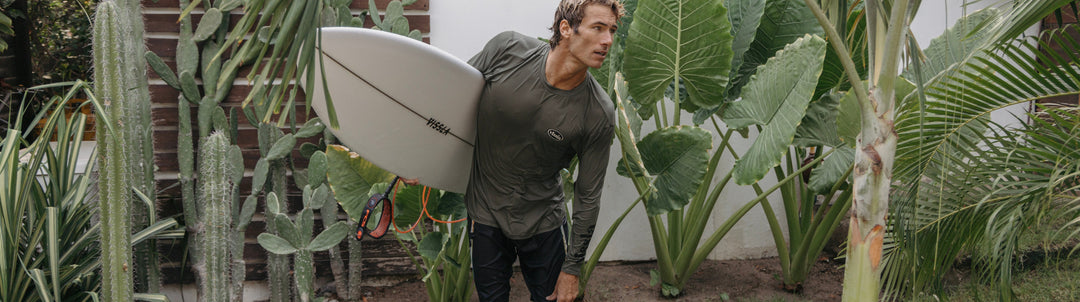 Andrew Jacobson running on a Mexican beach towards waves holding his board and wearing a Vissla wetsuit top