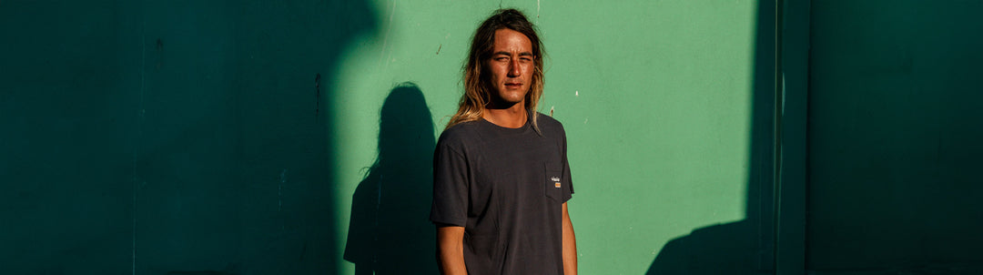Derrick Disney in front of a green wall inbetween shadows wearing a black Vissla Eco Tee Shirt