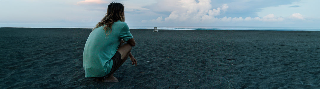 Derrick Disney in a Vissla Premium Tee sitting on a beach watching the waves