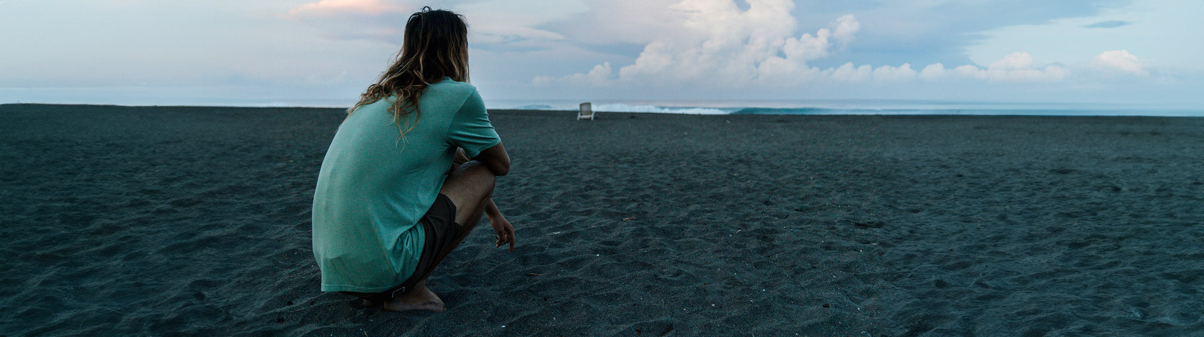 Derrick Disney in a Vissla Premium Tee sitting on a beach watching the waves