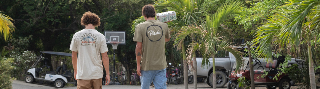 Two Vissla surfers walking away from the camera wearing Vissla graphic tees